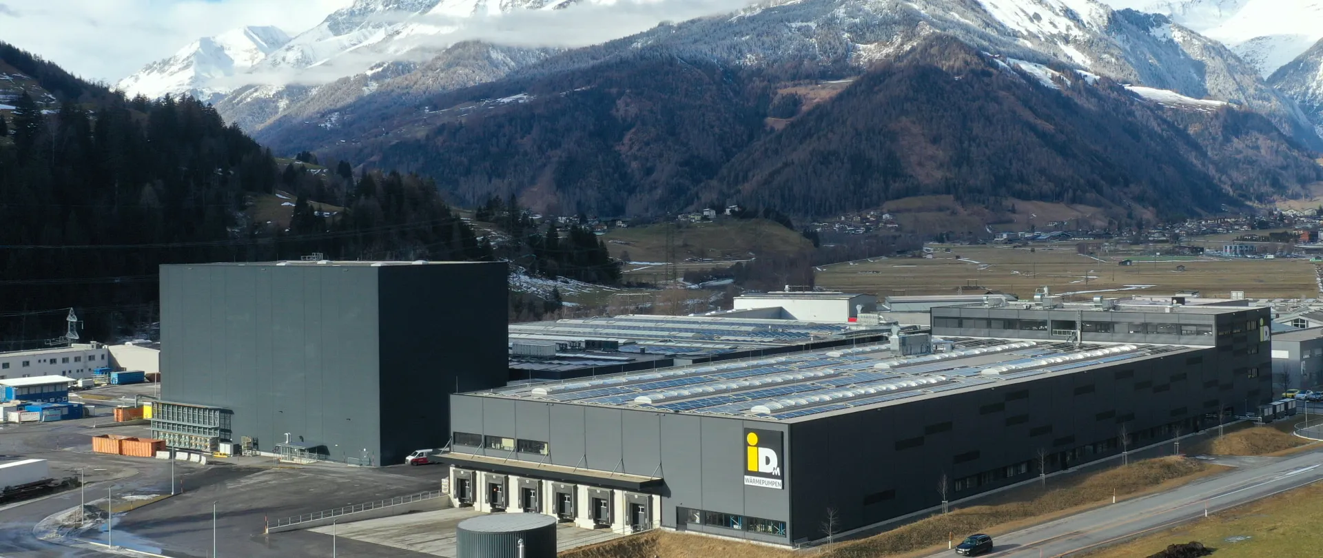 Produktions- und Logistikstandort von iDM Energiesysteme in Matrei in Osttirol mit Photovoltaikanlagen auf dem Dach – eingebettet in alpine Berglandschaft, Symbol für industrielle Innovationskraft und Nachhaltigkeit der Pletzer Gruppe.